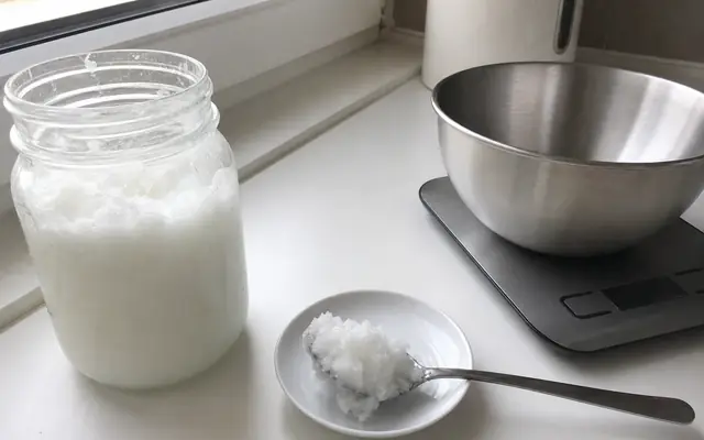 Otwarty słoik ze stałym białym olejem kokosowym i łyżka ze stali na białym blacie